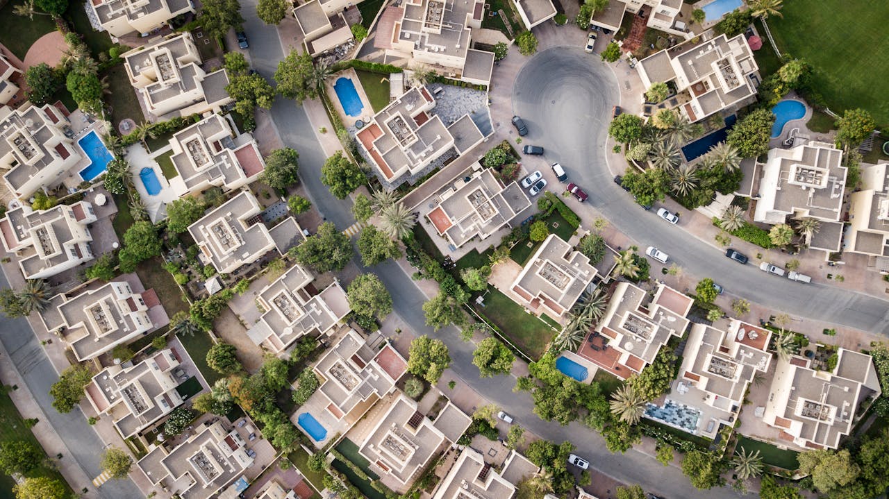 about-us-02 Explore a stunning aerial view of a residential area in Dubai with lush greenery and swimming pools.