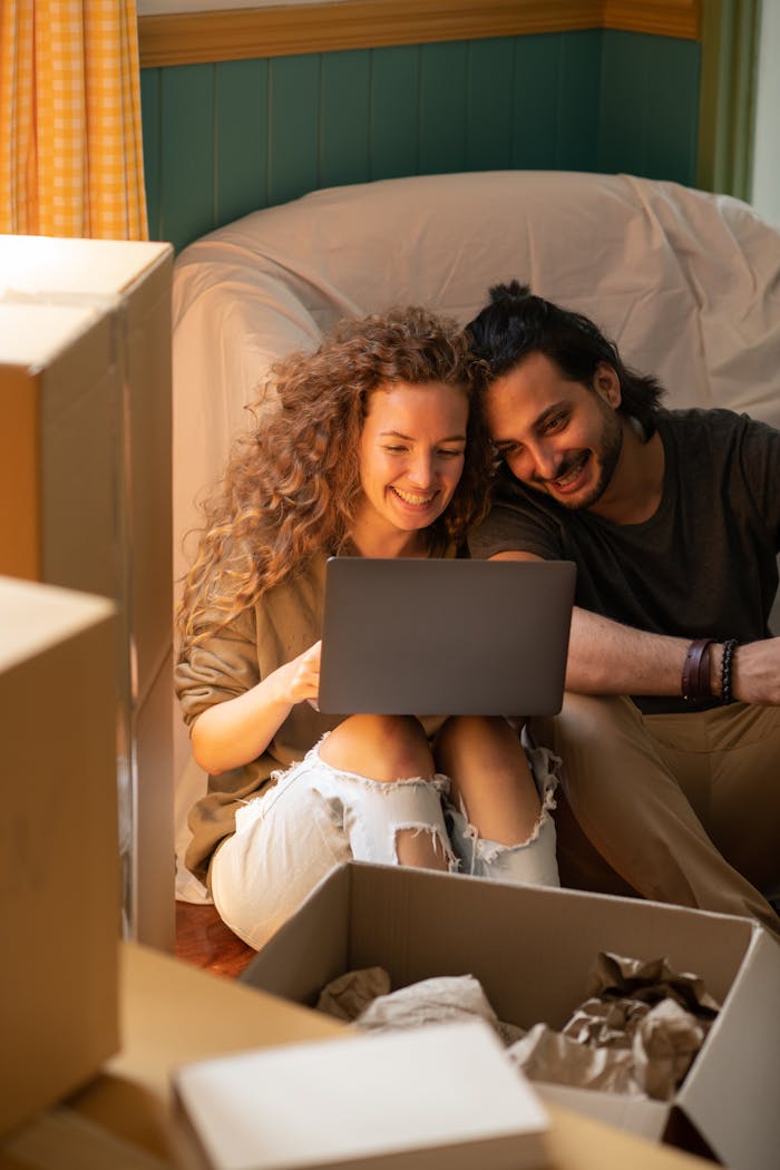 Mastering the First Impression: Your intriguing post title goes here Smiling couple using laptop while unpacking boxes in their new home. Bright, cozy indoor setting perfect for relocation themes.
